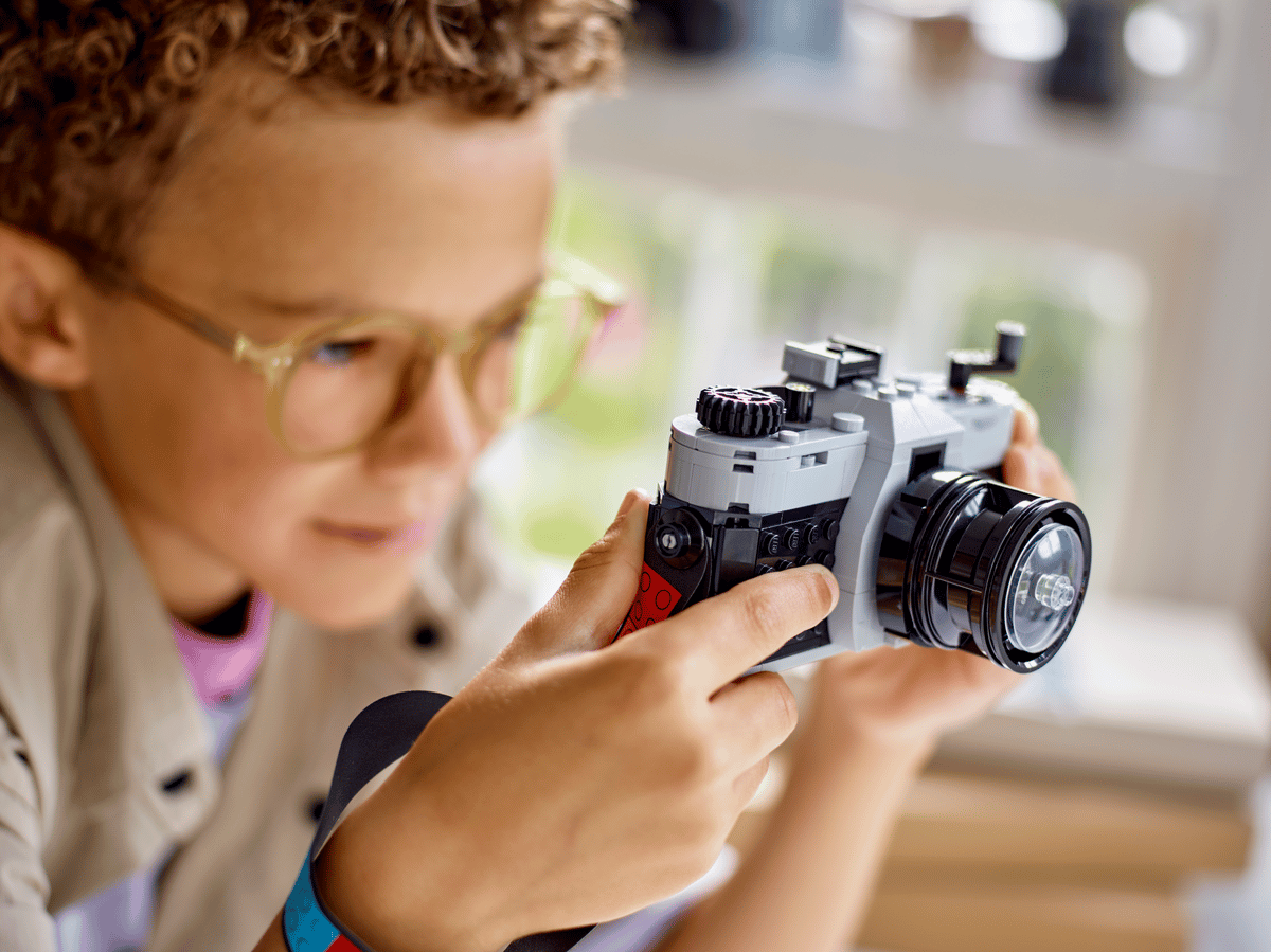 Barn med briller holder en LEGO-kamera, perfekt leke for kreative barn og fotografi-entusiaster.