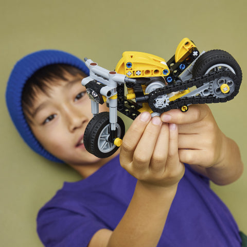 Barn holder gul LEGO Technic motorsykkel med kjede og hjul, perfekt leketøy for barn