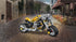 Gul LEGO Technic motorsykkel på steinlagt gate med kaféer i bakgrunnen