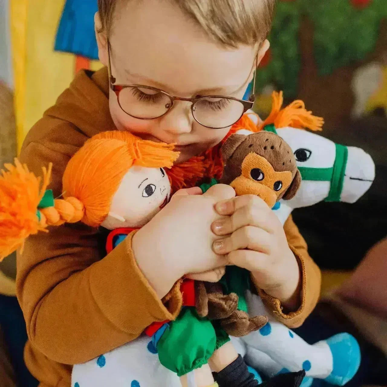 Barn med briller klemmer Pippi Langstrømpe dukke, apebamse og hest i lekemiljø.